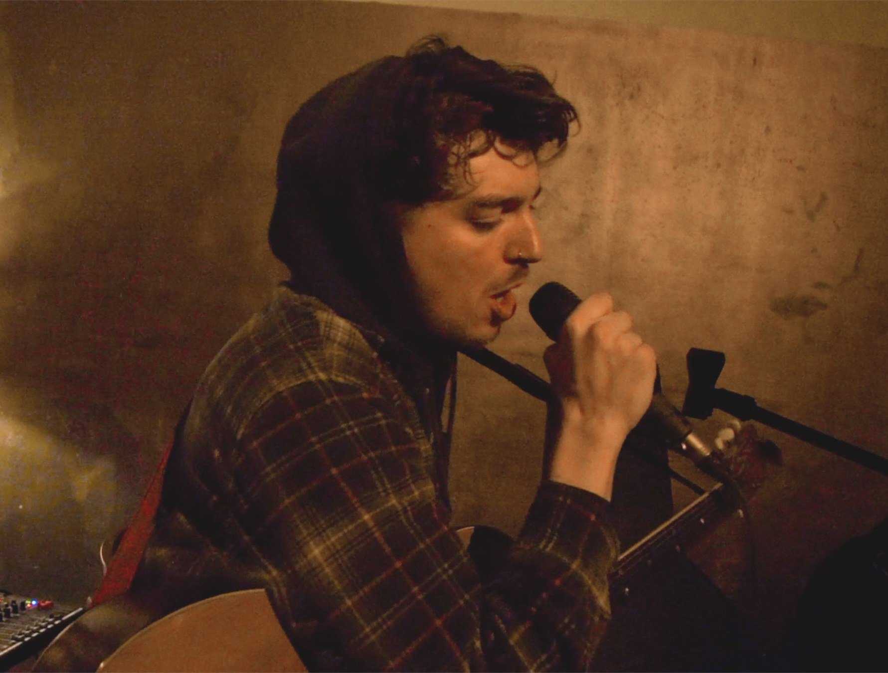 Robin Fisher singing into a microphone while playing guitar.