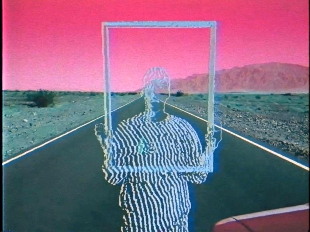A distorted figure holding an empty frame on a desert road beneath a vivid pink sky.