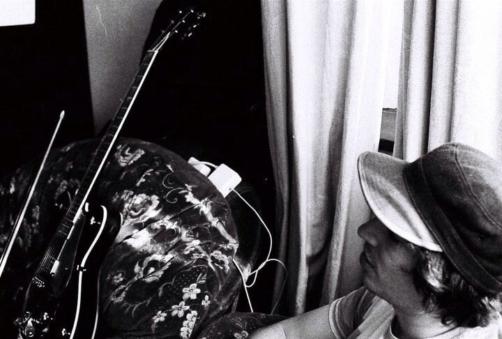 Robin Fisher seated beside a guitar at home in a black-and-white photograph.